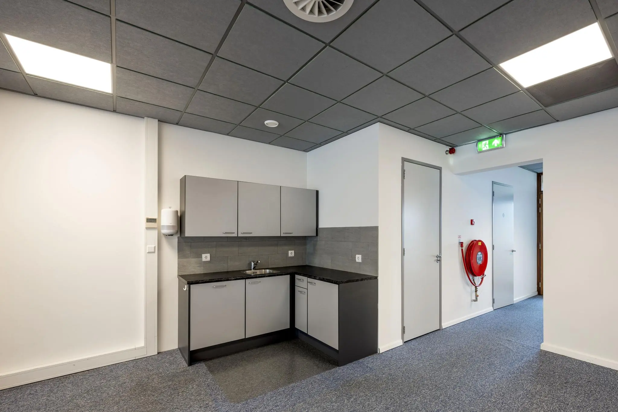 Kleine keukenhoek in een modern kantoor aan de De Ruijterkade met brandhaspel en nooduitgang.